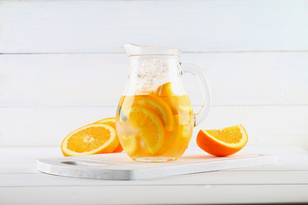 Orange detox water in a jug on a white wooden table. Healthy food, drinksの写真素材