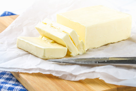 A bar of butter on a wooden board with a knife, on a white table. Ingredients for cookingの写真素材
