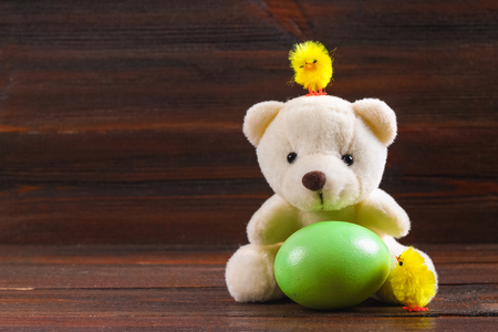 White teddy bear with a green Easter egg and chickens on a brown wooden tableの写真素材