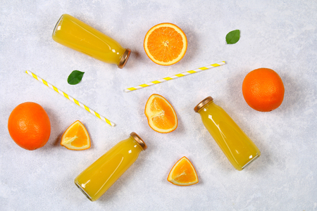 Glass bottles with fresh orange juice with orange slices and yellow tubes on a light gray table. Top view. Flat Layの写真素材