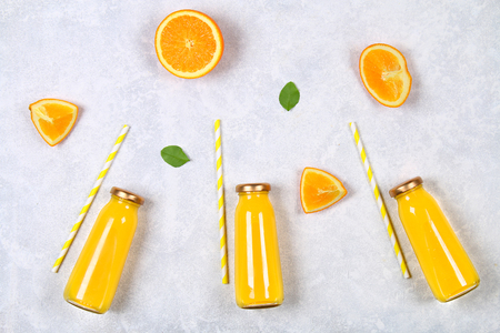 Glass bottles with fresh orange juice with orange slices and yellow tubes on a light gray table. Top view. Flat Layの写真素材