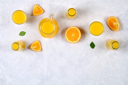 Glass bottles, glasses and a pitcher of fresh orange juice with slices of orange and yellow tubes on a light gray table. Top view. Flat Layの写真素材
