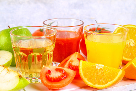 Glasses with fresh orange, apple, tomato juice on a gray concrete table. Lobules Fruits and vegetables aroundの写真素材