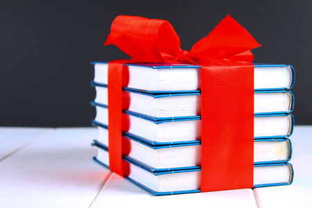 A pile of books tied with a red ribbon on a white wooden table. A gift on the background of a chalkboardの写真素材