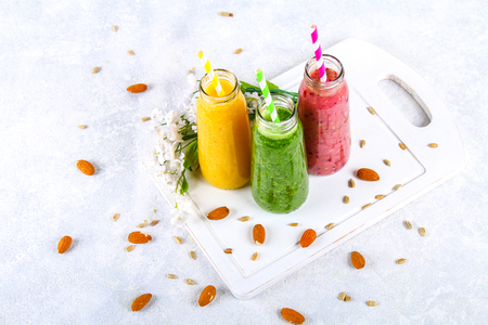 Green, yellow, purple smoothies in bottles of berries, greens, oranges on a white board on a gray tableの写真素材
