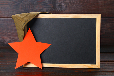 Chalkboard with empty space, military cap and red star on a wooden table. Day of the defender of the fatherland and May 9の写真素材