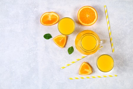 Glass bottles, glasses and a pitcher of fresh orange juice with slices of orange and yellow tubes on a light gray table. Top view. Flat Layの写真素材