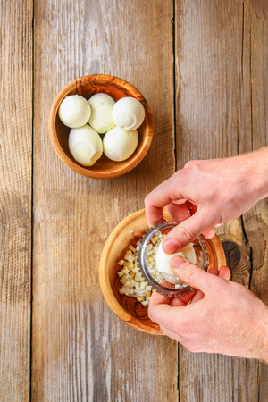 Male hands force the boiled chicken eggs through a vegetable cutter for okroshki on an old wooden table. Cutting eggsの写真素材