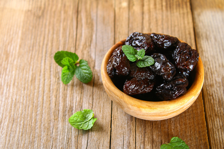 Prunes with mint leaves in a bowl on an old wooden tableの写真素材