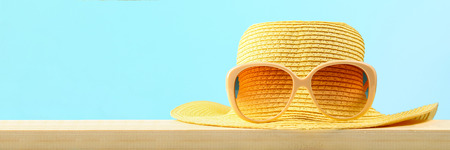 Yellow sunglasses and hat on a wooden shelf on a blue pastel background. Minimalismの写真素材