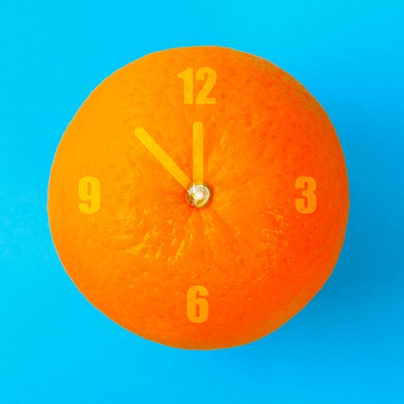 A clock in the form of an orange on a blue pastel background. Minimalism. The concept of summer, timeの写真素材