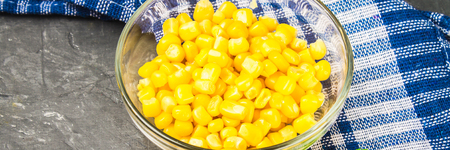 Canned corn in a glass plate on a gray concrete background