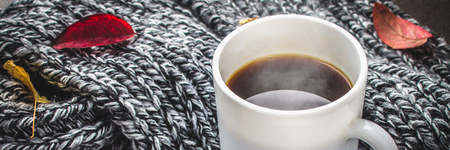Mug of hot coffee in autumn setting on a wooden table with a knitted scarf, sweater. Comfort,...