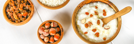 Rice milk porridge with nuts and raisins in wooden bowls on a white wooden tableの写真素材