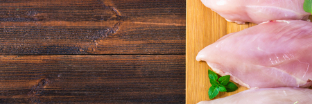 Raw chicken fillets on a cutting board against the background of a wooden table. Meat ingredients for cooking. Empty place for an inscription. Copy the space. Flat lei. Top viewの写真素材