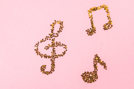 Musical notes of starry golden confetti lying on a pink pastel backgroundの写真素材