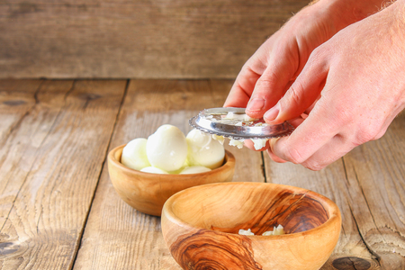 Male hands force the boiled chicken eggs through a vegetable cutter for okroshki on an old wooden table. Cutting eggsの写真素材