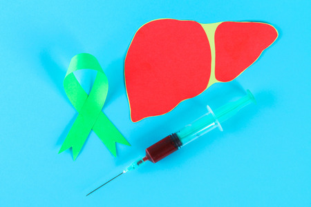 World Hepatitis Day. June 28th. A green jade ribbon, a syringe with blood and a liver on a blue tableの写真素材