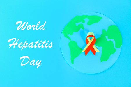 World Hepatitis Day. June 28th. Red yellow ribbon, planet Earth on a blue tableの写真素材