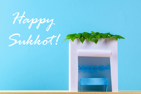 Text of Happy Sukkot. A hut made of paper covered with leaves on a blue background. Postcard, congratulationsの写真素材