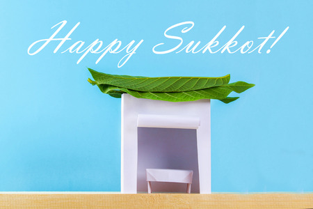 Text of Happy Sukkot. A hut made of paper covered with leaves on a blue background. Postcard, congratulationsの写真素材