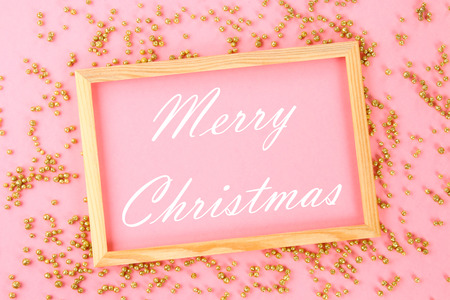 Merry Christmas. A wooden empty frame on a pastel background surrounded by shiny decorative stars...