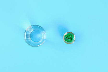 Swallowing tablets. Pills and a glass of water against a blue table background. Top view, copy space, flat layの写真素材