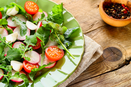 Vegetarian salad of arugula, tomato, radish and mozzarella cheese on an old wooden tableの写真素材