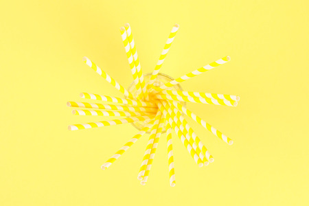 Yellow striped straw paper tubes on a bright yellow pastel background. Top view, copy spaceの写真素材