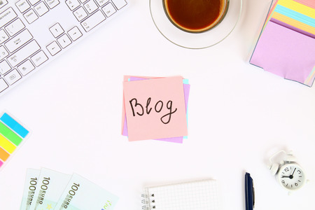 Text blog on a sticker note on a white desktop next to a coffee mug and a keyboard. Top view, flat layoutの写真素材