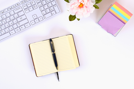 A blank white notepad on a white desktop next to a coffee mug and a keyboard. Top view, flat layout. Copy the spaceの写真素材