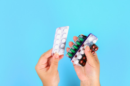 The girl holds in her hands blisters of various tablets and pills on the background of a blue table....