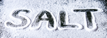 The word salt is written on small crystals of salt scattered on a black tableの写真素材