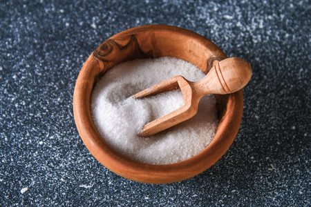 Crystals of shallow salt in a wooden bowl on a dark gray table. Background for advertising salt. Table salty. Salted foodの写真素材