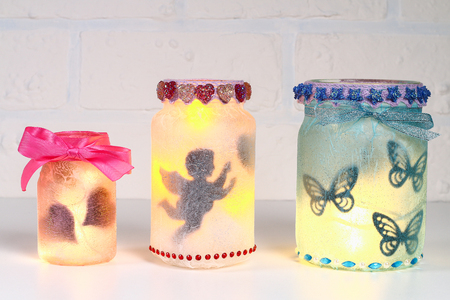 Diy Fairy Jar on white brick wall background. Gift ideas, decor St February 14, Valentines Day, love, wedding. Handmade Lamp, night light, lantern from glass jar, napkin, glue, glitterの写真素材