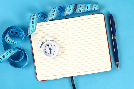 Healthy lifestyle concept with notepad. Weight loss or diet concept. Calculator, clock, measure tape on a blue table background with copy space for design. Top view.の写真素材