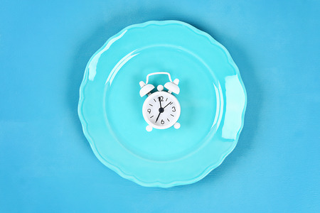 White alarm clock in blue empty plate. Top view. Time to lose weight , eating control or time to diet concept.の写真素材