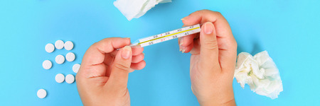 A man holds a thermometer in his hand with a high temperature against a blue table with tablets. Top view, copy space, flat layの写真素材