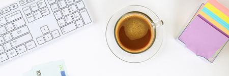 Calculator, euro banknotes, blank notebook on a white desktop next to a coffee mug and a keyboard. Top view, flat layout. Copy the spaceの写真素材