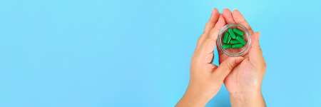 Banner. The girl holds in her hands blisters of various tablets and pills on the background of a blue table. Top view, copy space, flat layの写真素材