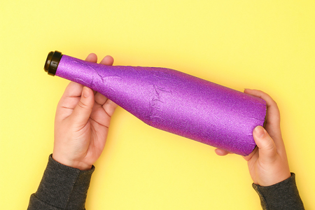 Diy Mardi Gras bottle purple self adhesive paper, green bead, carnival mask, sequins yellow background. Gift idea, decor Mardi Gras, Fat, Shrove Tuesday. Step by step. Top view. Process children craftの写真素材