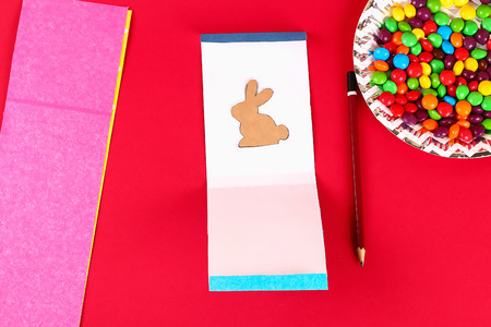 Diy Easter wrapping package sweets in a bag with a cut out bunny silhouette on a red background....