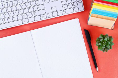 Blank notebook on the coral background, plant, keyboard. Top view, flat lay. Mockup, copy space.の写真素材