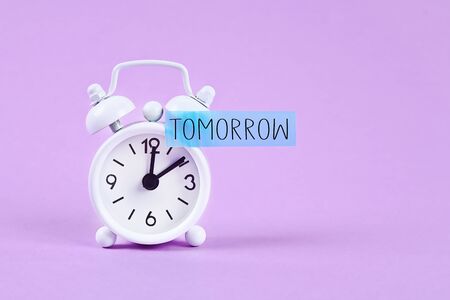 Procrastination, delay and urgency concept. White alarm clock with a sticky note with text tomorrowの写真素材
