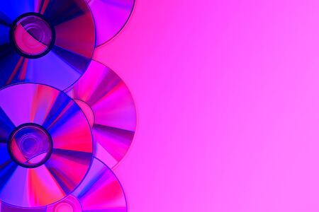 Piles of old and dirty CDs,DVD on pink violet purple neon background. Used and dusty disk with copy space for add textの写真素材