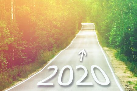 Concept for new year 2020. Word 2020 written on highway road in the middle of empty asphalt road at golden sunset.の写真素材