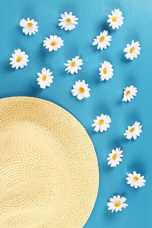 Straw hat with a camomile on a blue background. Top view. Summer background. Flat lay.の写真素材