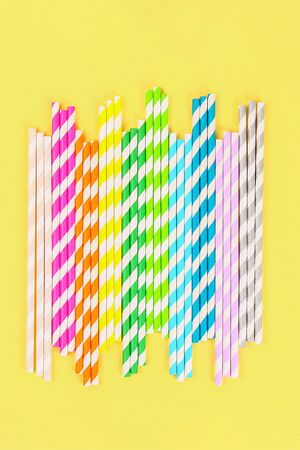 Multi-colored straw paper tubes on a bright yellow pastel background. Top view