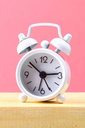 White small alarm clock on a wooden shelf on pink pastel background. Minimalismの写真素材