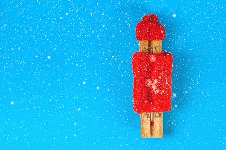 Wooden thermometer, wearing a red hat and sweater on a blue background. The concept of cold, frost,...